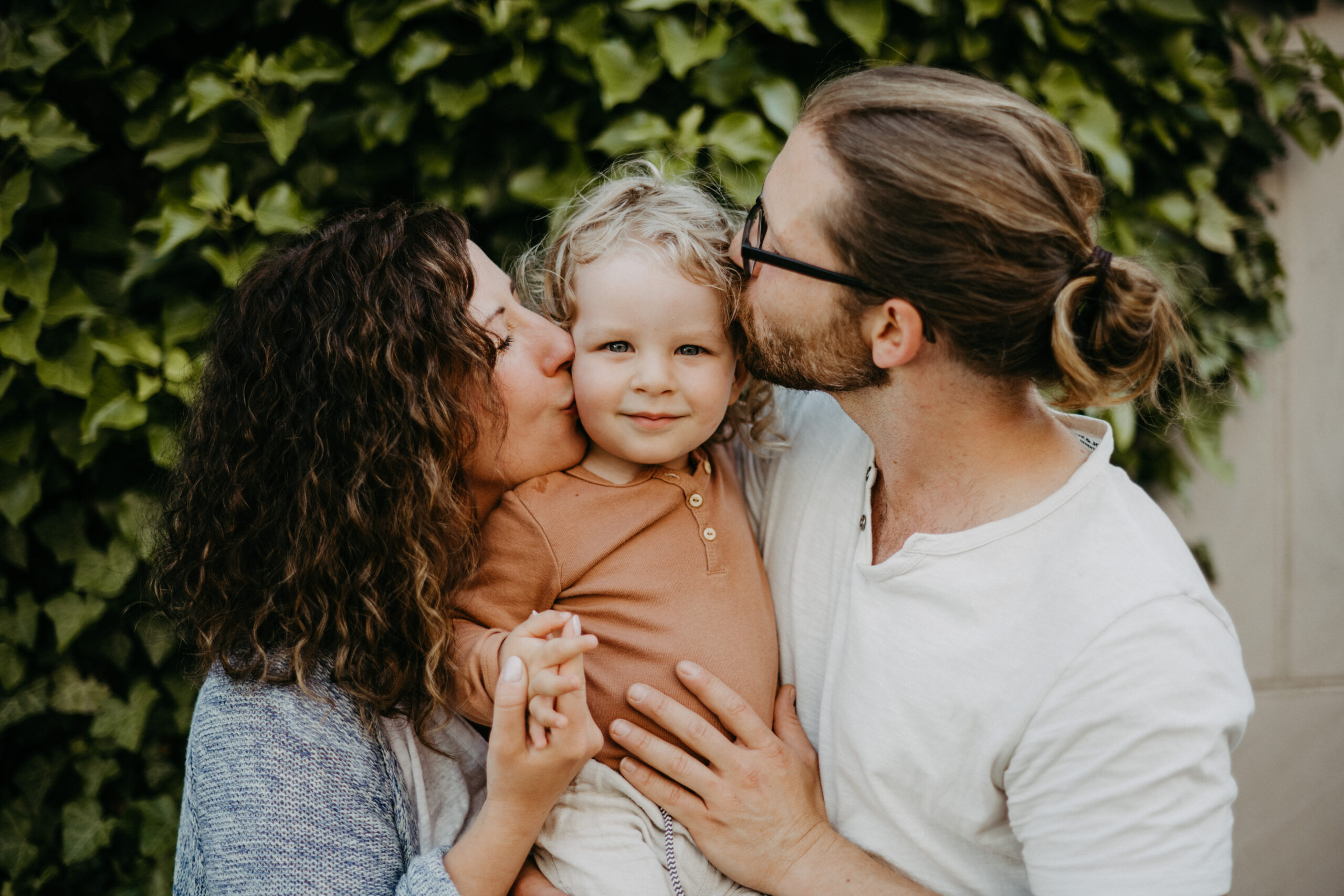 Familien-Fotoshooting bei dem die Eltern ihr Kind von beiden Seiten gleichzeitig auf die Wange küssen, fotografiert von Familienfotografin Daria Lanzet aus Bonn