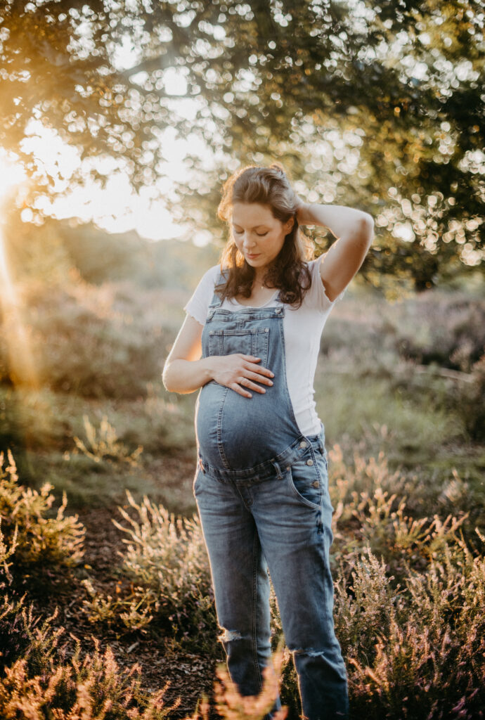 Portrait einer Schwangeren, die sich in Gedanken den Bauch hält und ihre haare aus dem Gesicht streicht beim Babybauchfotoshooting in Köln