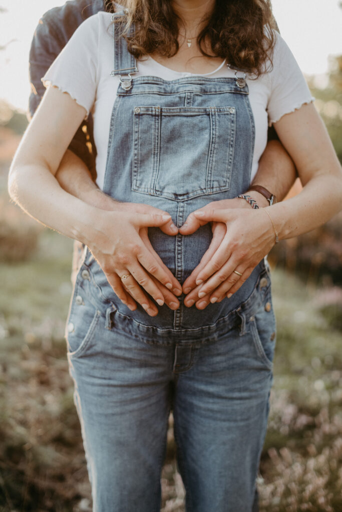 Detailfoto der Hände beider Eltern, die auf dem Babybauch ein herz formen beim Babybauchfotoshooting in der Warner Heide 