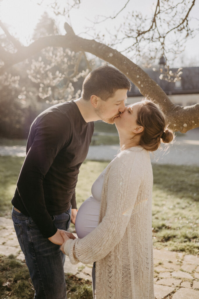 Paar steht sich beim Schwangerschafts-Fotoshooting gegenüber und küsst sich. Es ist Winter.