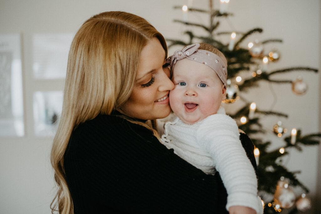 Mutter küsst ihr Baby vor dem Weihnachtsbaum beim Weihnachtsmarkt-Fotoshooting für Familien in Bonn