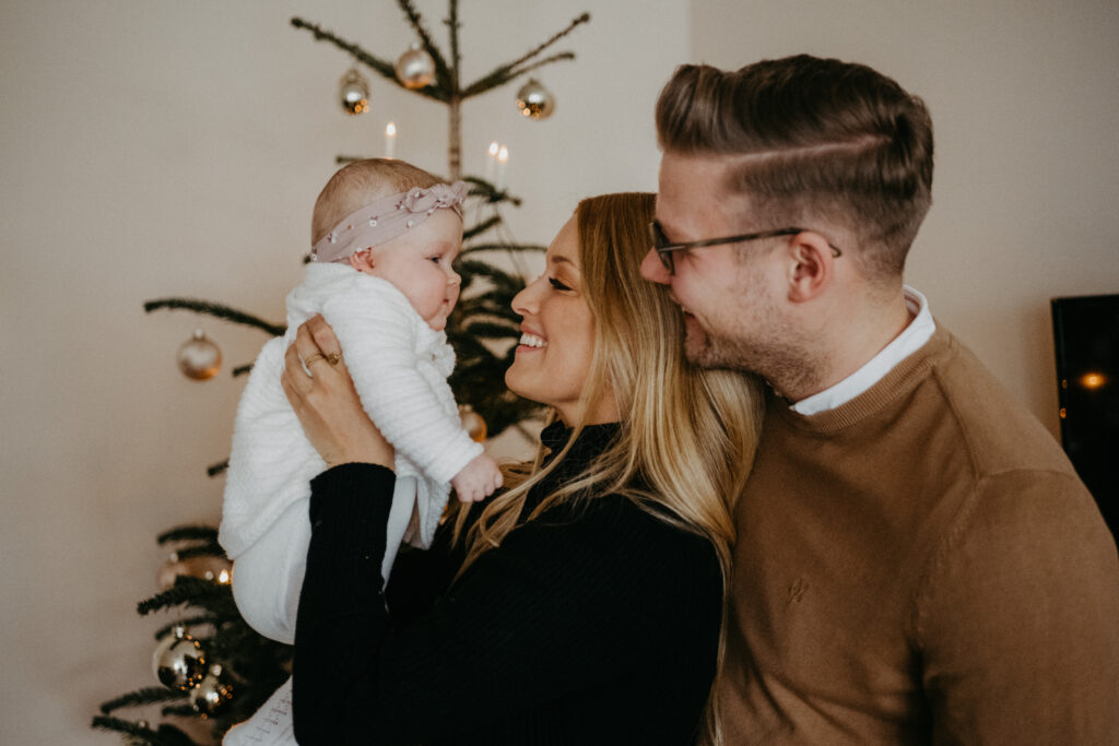 Eltern spielen mit ihrem Baby vor dem Weihnachtsbaum beim Weihnachtsmarkt-Fotoshooting für Familien in Bonn