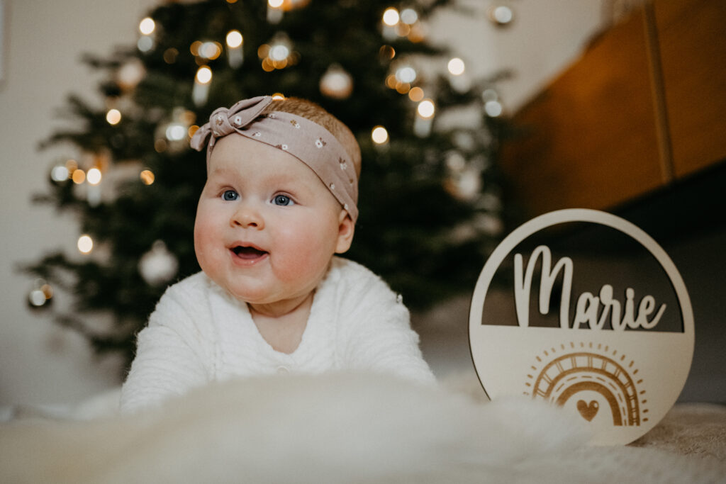 Baby liegt beim Fotoshootings vor dem Weihnachtsbaum auf dem Bauch und freut sich und lacht