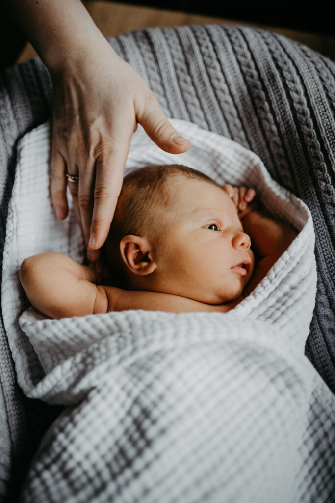 Die Mutter streichelt sanft den Kopf des neugeborenen Babys, während es in ein Tuch eingewickelt ist beim neugeborenen-Fotoshooting