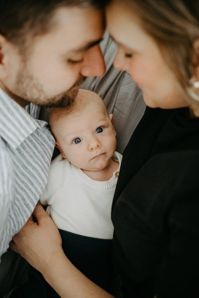kleines baby schaut neugierig zwischen seinen Eltern hindurch beim New Born Fotoshootings in Rheinbach