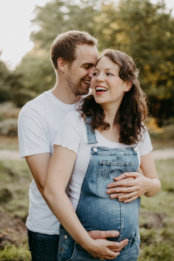 Schwangerschaftsshooting in der Wahren Heide. Das Paar geht Hand in Hand im Sonnenuntergang  spazieren, sie trägt ein Latzhose.